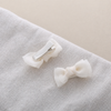 White bow hair clips for girls displayed on textured fabric