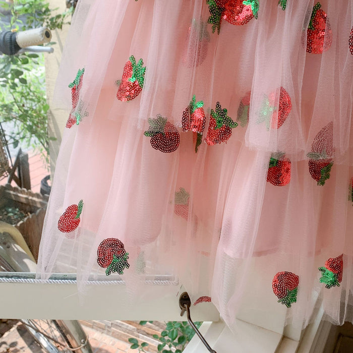 Layered pink tulle skirt with red and green sequin strawberry motifs, close-up of the dress hem