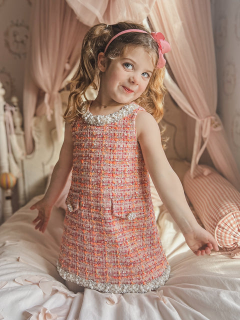 Girl wearing pink bouclé tweed dress on bed – perfect birthday or wedding flower girl outfit